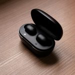 HomePage Stylish black wireless earbuds displayed in an open charging case atop a wooden table.